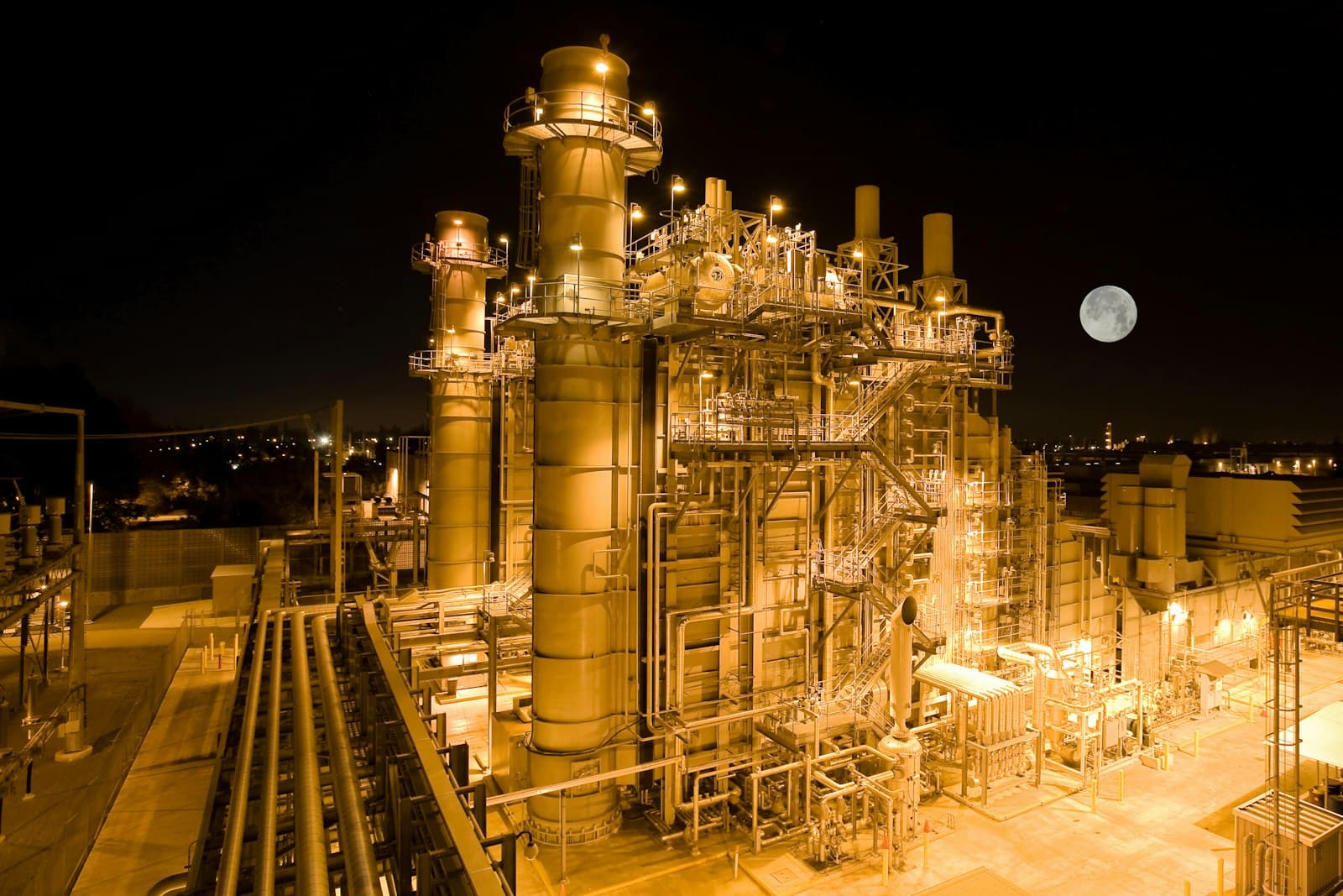 A power plant lit up at night under a full moon
